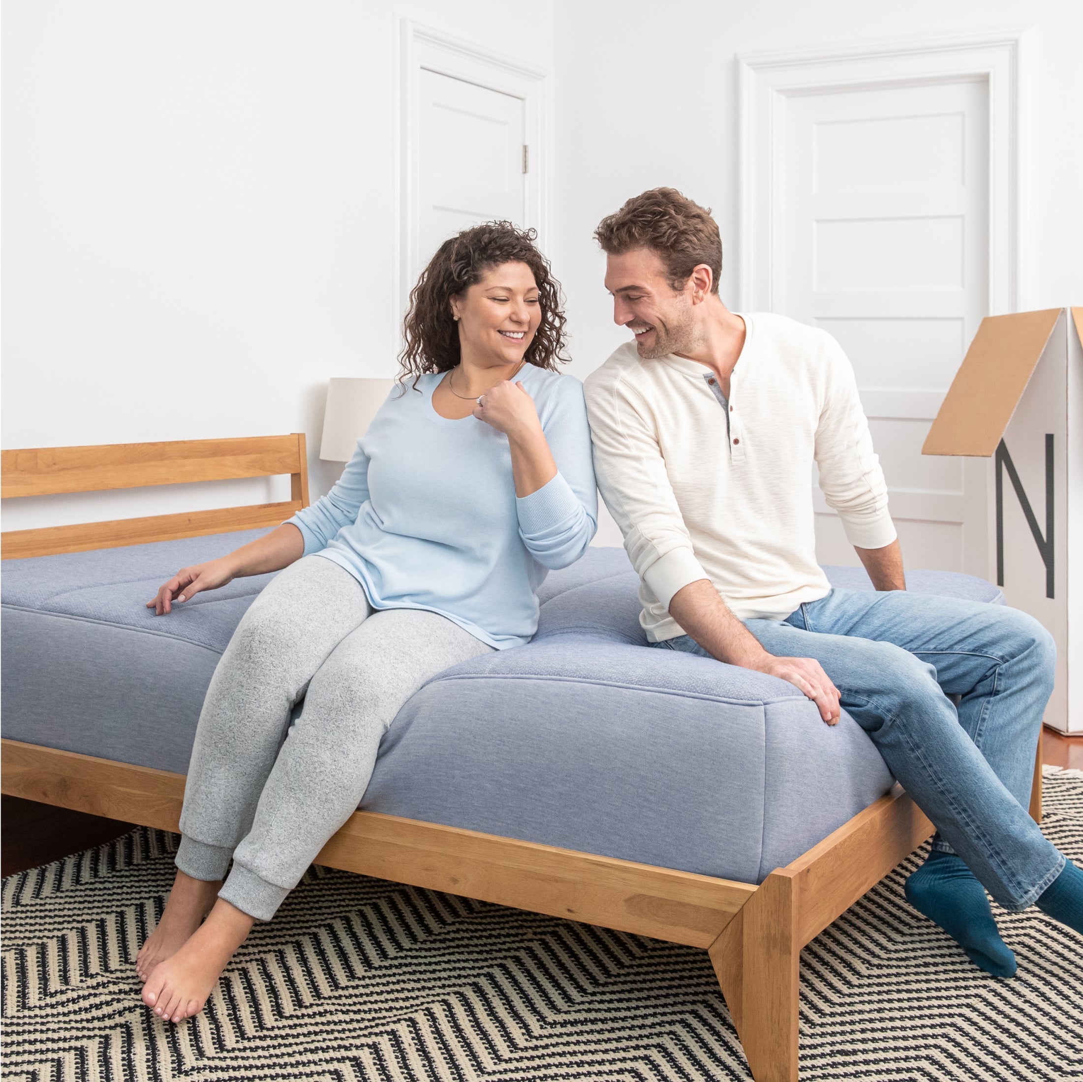A couple sitting on the Tuft and Needle Legacy Hybrid Mattress in a bedroom