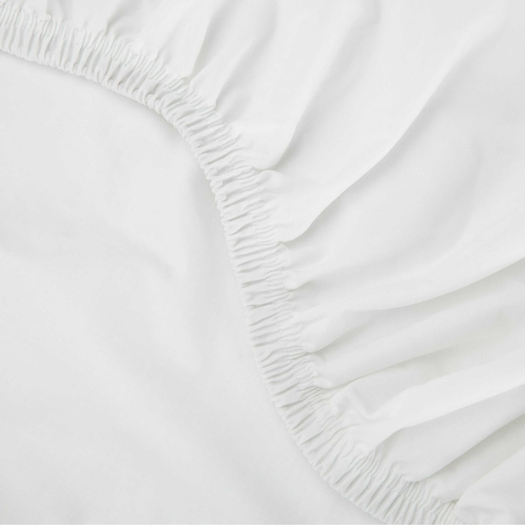 Tuft & Needle Close-up of a white fitted sheet with elastic waistband on a bed.